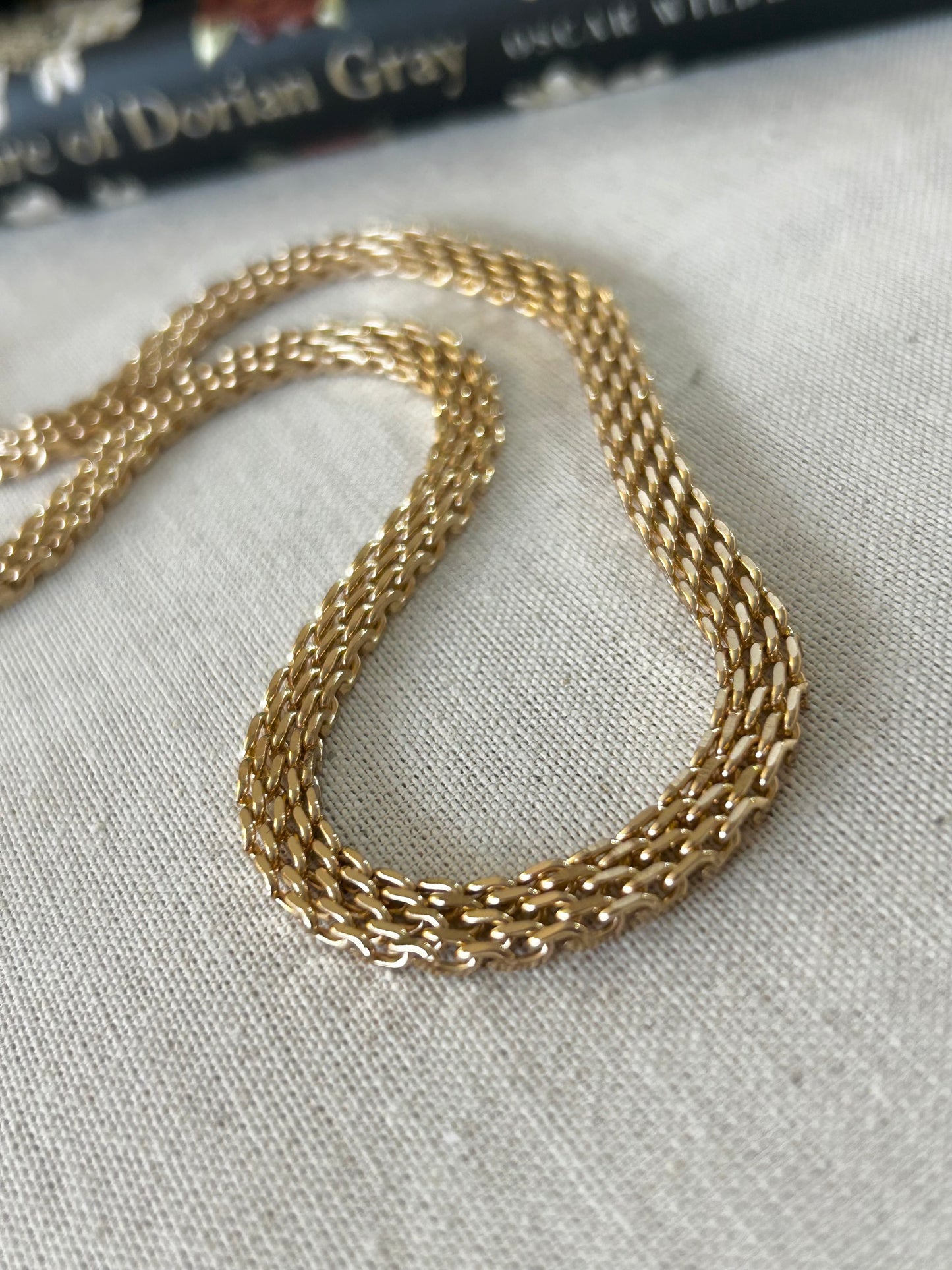 Gold chain on a textured fabric surface with a book in the background