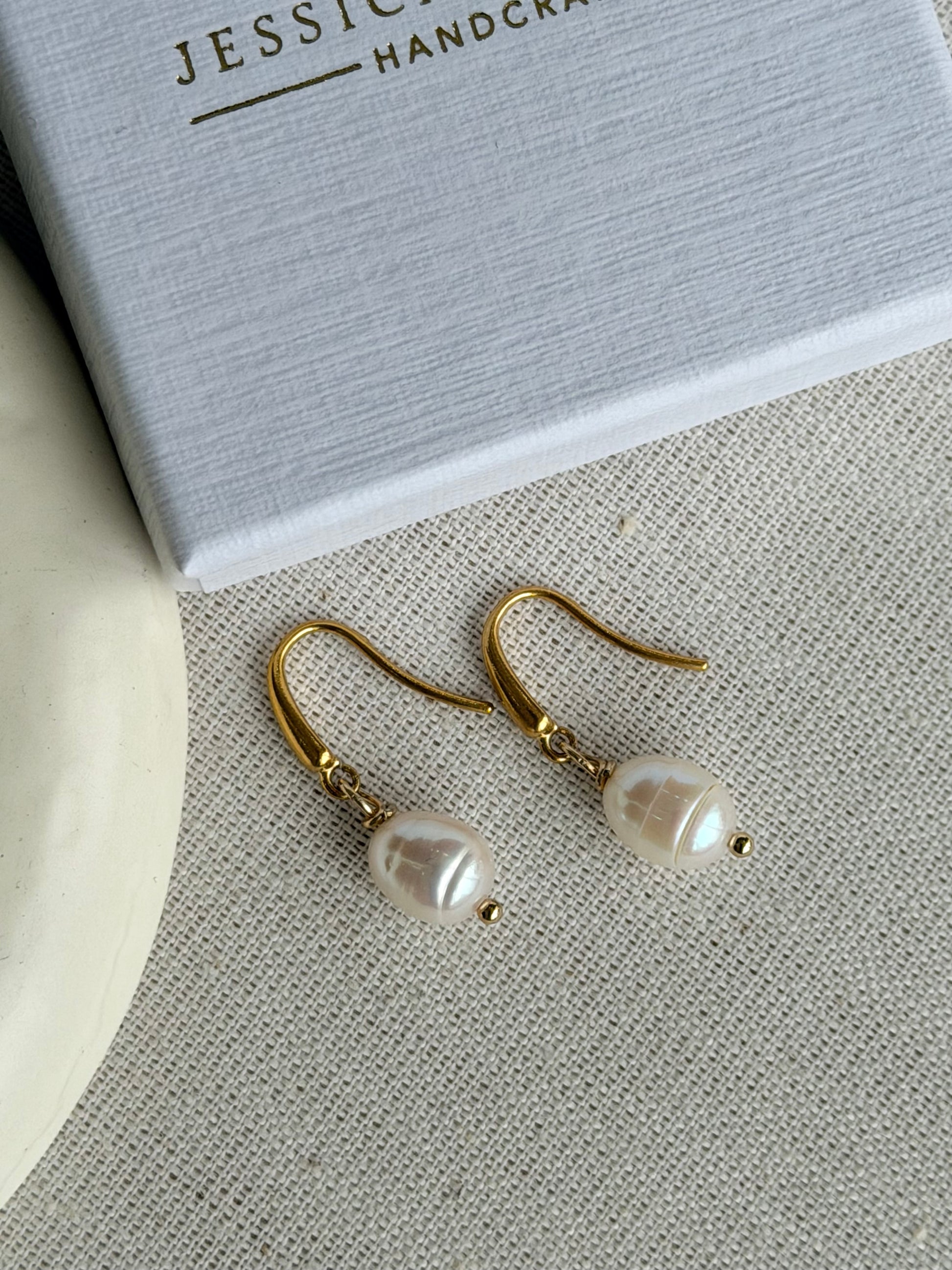Pearl earrings on a textured surface with 'Jessica and James handcrafted' box in the background