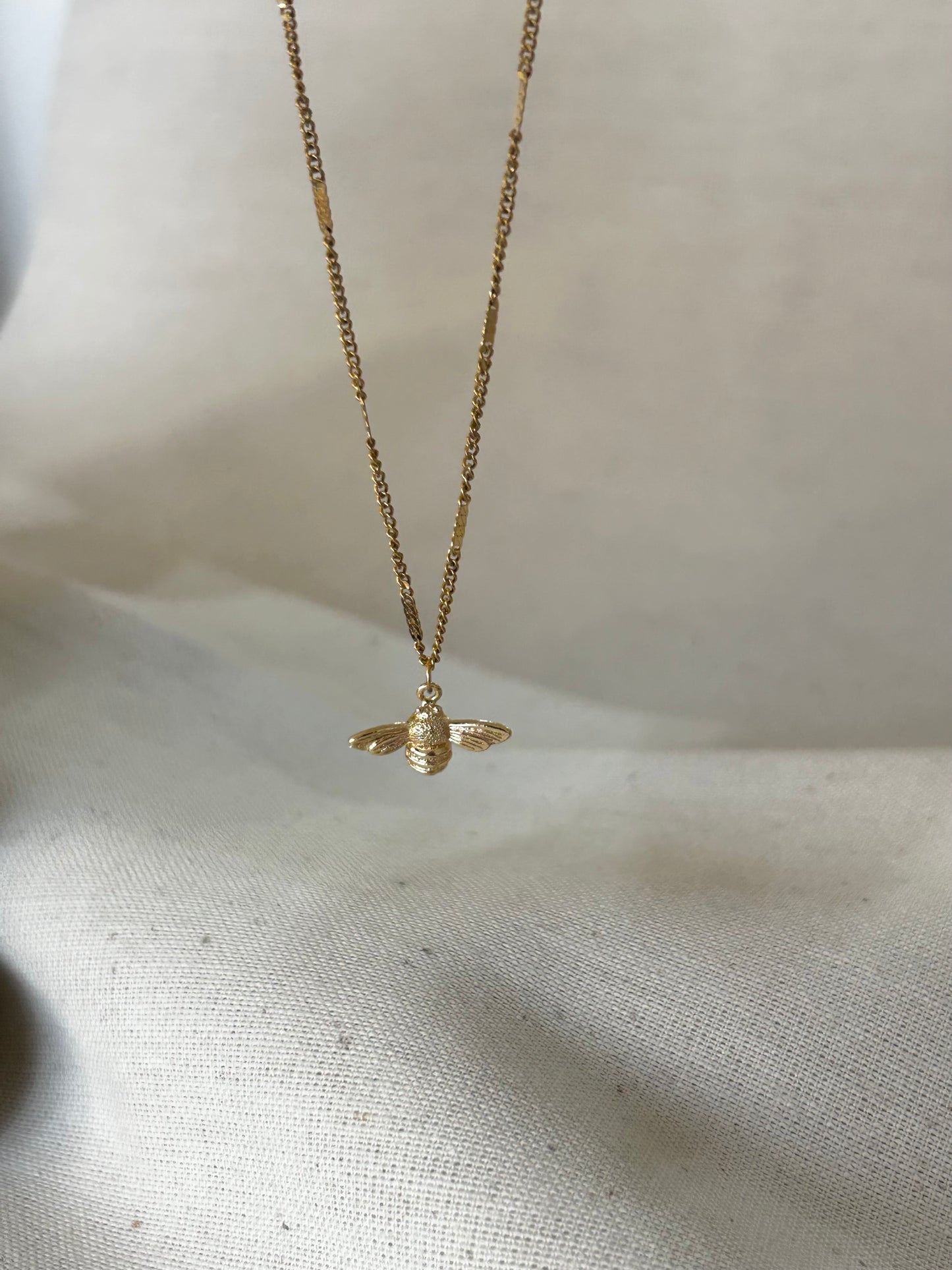 Gold bee necklace on a light fabric background