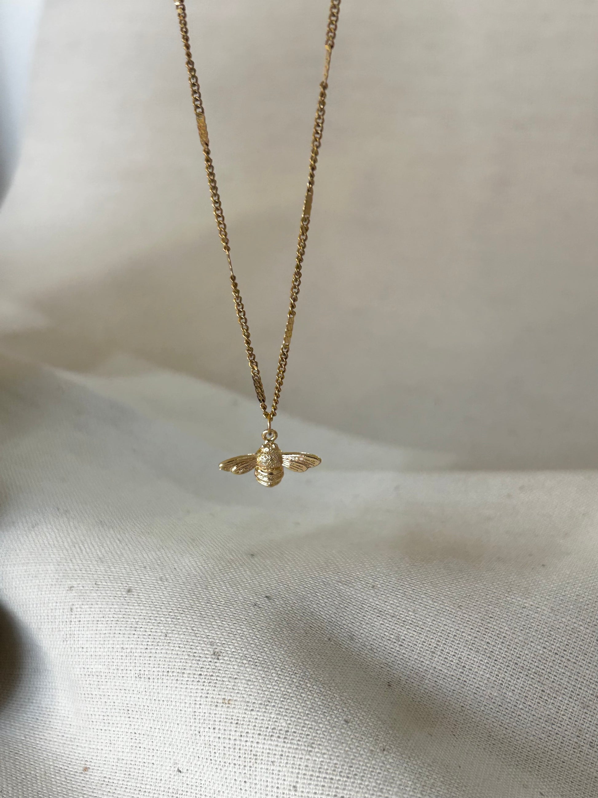 Gold bee necklace on a light fabric background