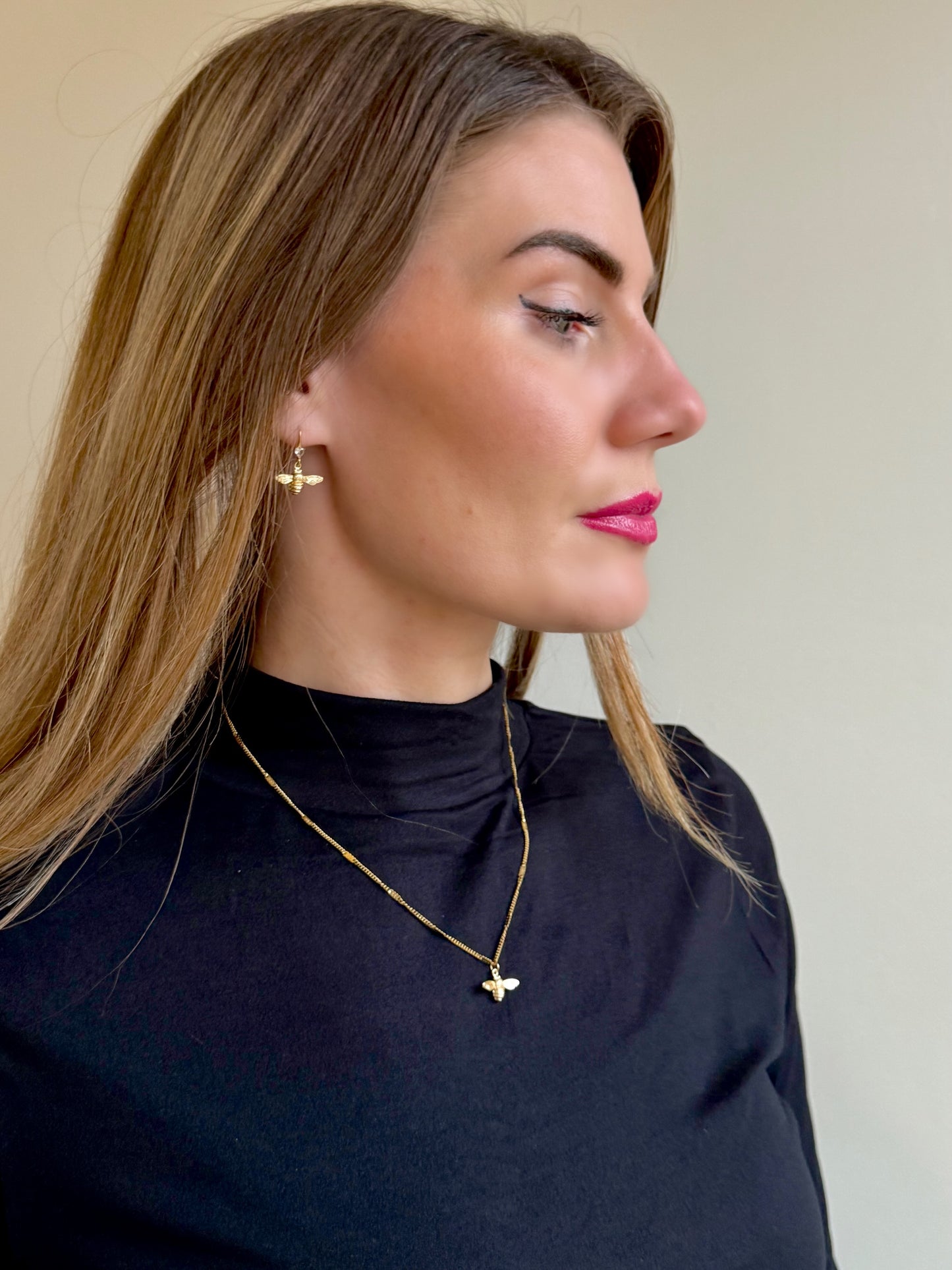 Woman wearing gold bee earrings and a bee necklace against a neutral background