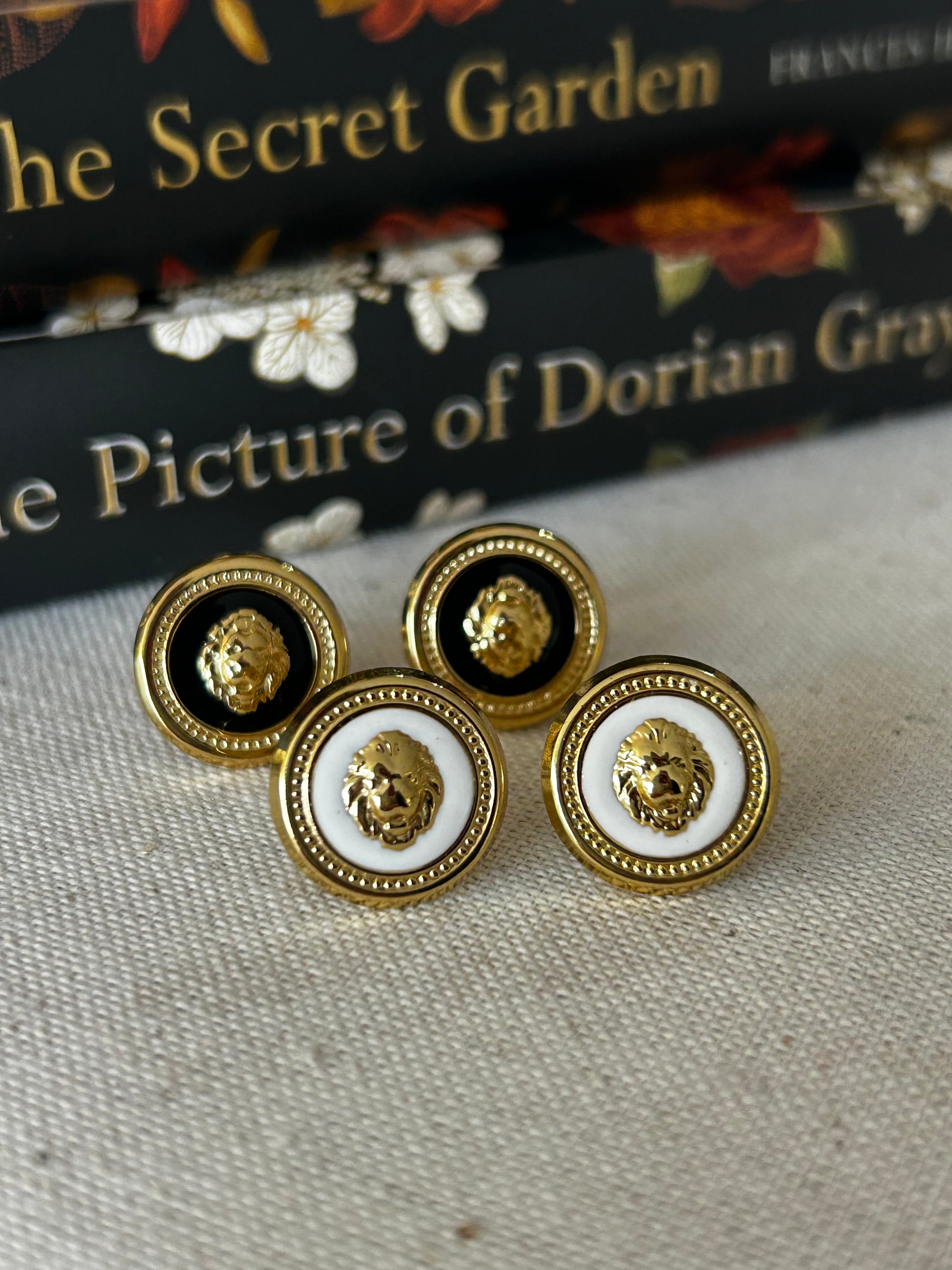 Gold and black button earrings on a textured surface with books in the background