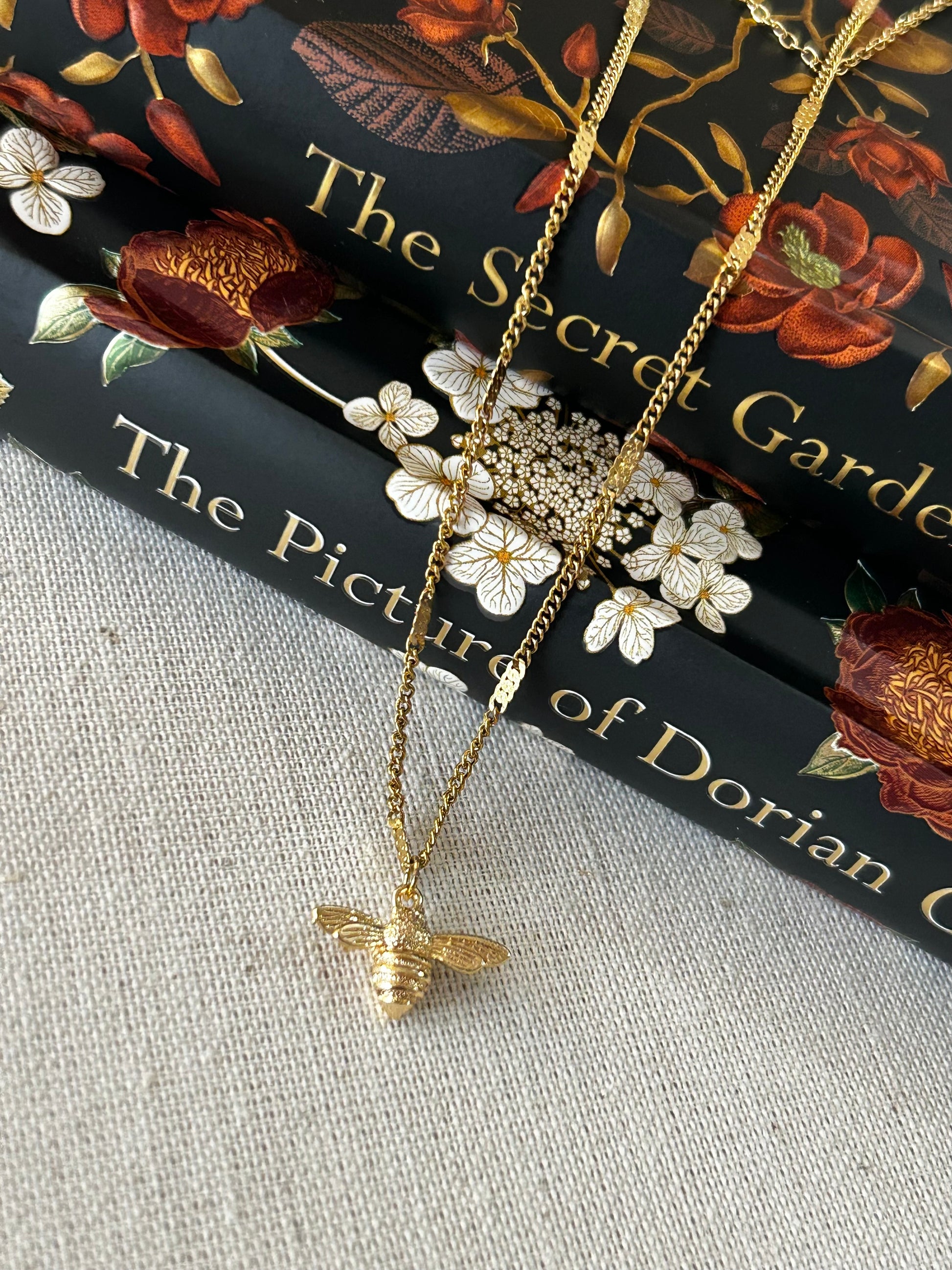 Gold bee necklace on a book with floral design