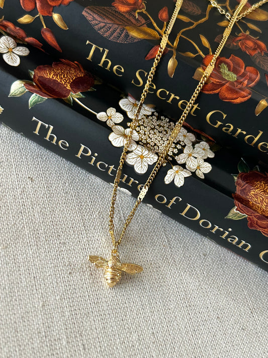 Gold bee necklace on a book with floral design