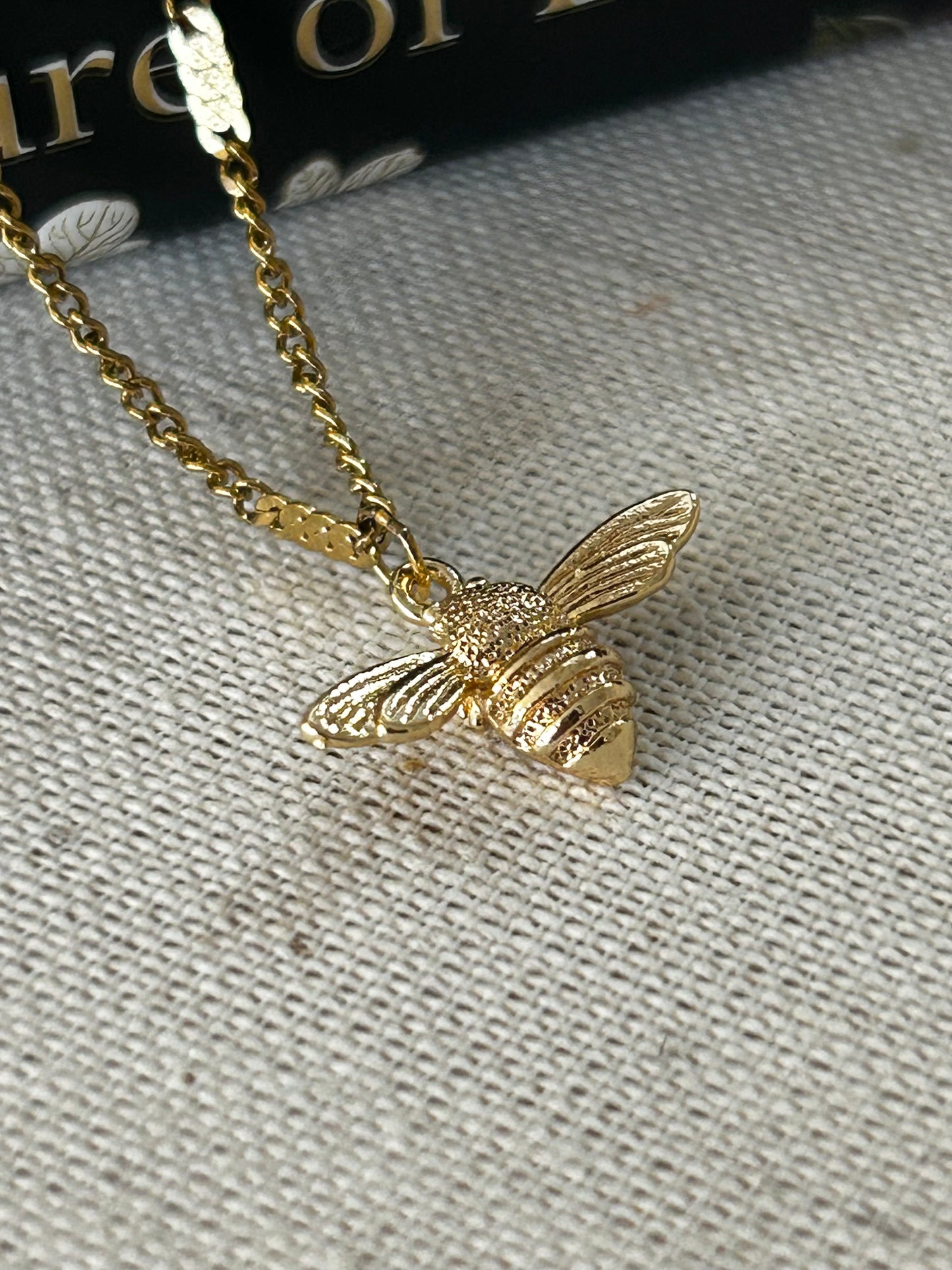 Gold bee-shaped pendant on a chain against a textured gray background