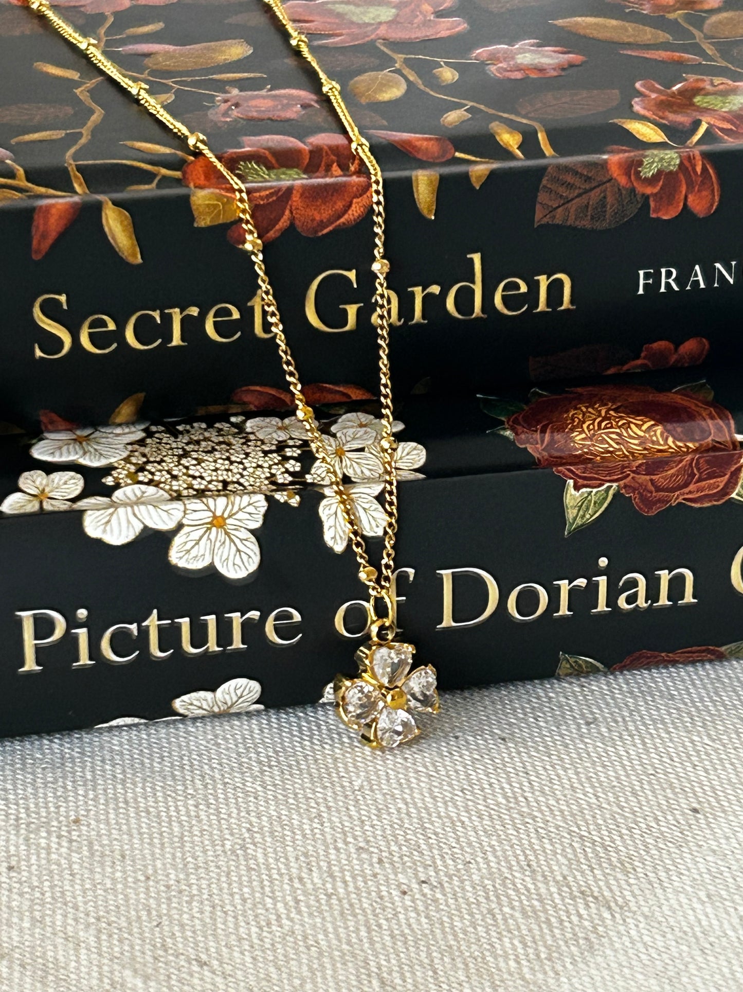 Gold necklace with floral pendant on a book titled 'Secret Garden' by Frances Hodgson Burnett.