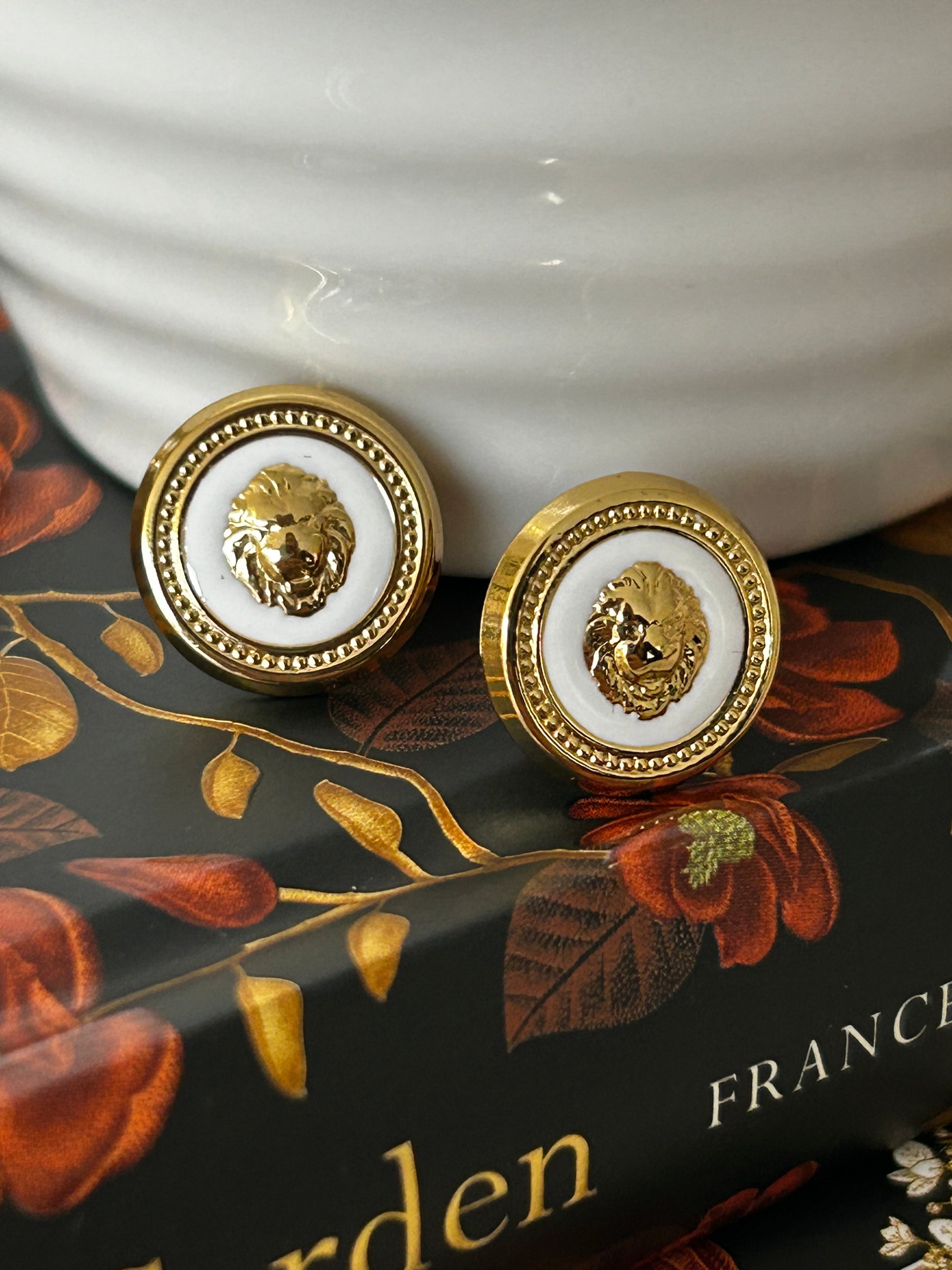 Close-up of decorative lion head button earrings with floral design in the background