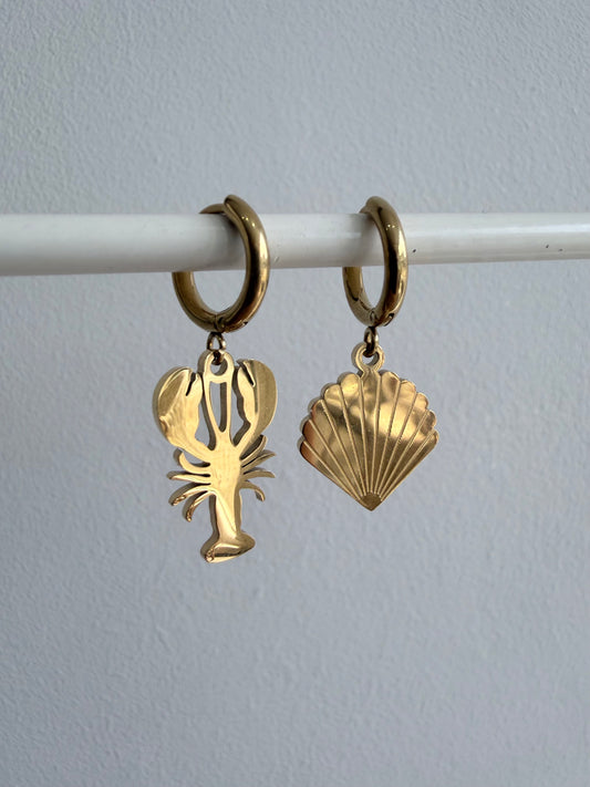 Gold hoop earrings with lobster and shell charms on a white rod against a light gray background
