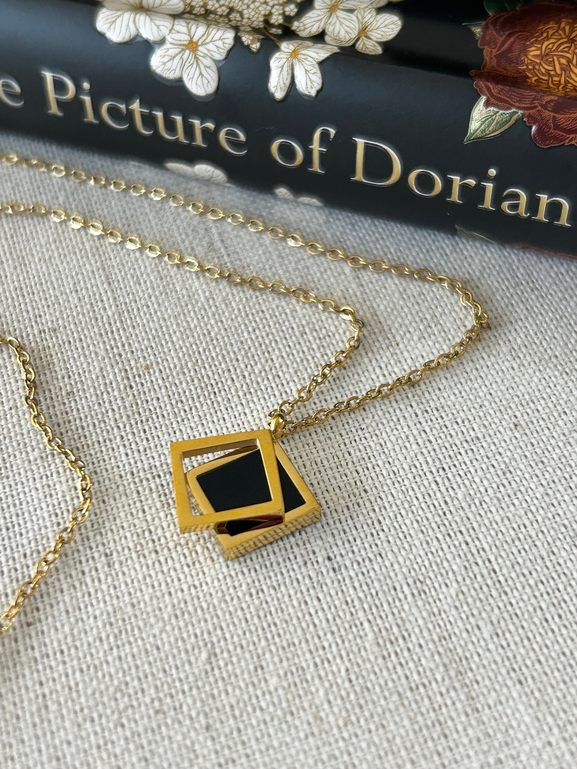 Gold necklace with a black pendant on a textured surface with 'The Picture of Dorian' book in the background.