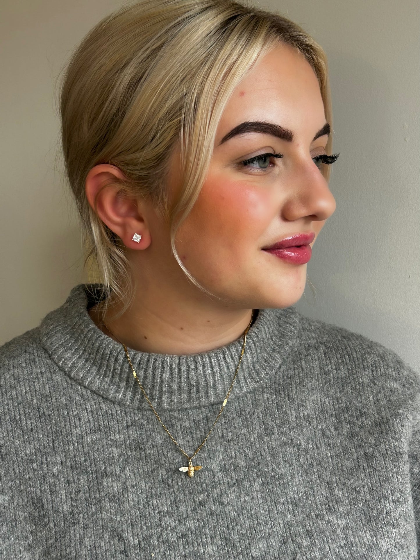 Woman wearing a gray sweater with a neutral background modelling Jessica and James jewellery bee necklace
