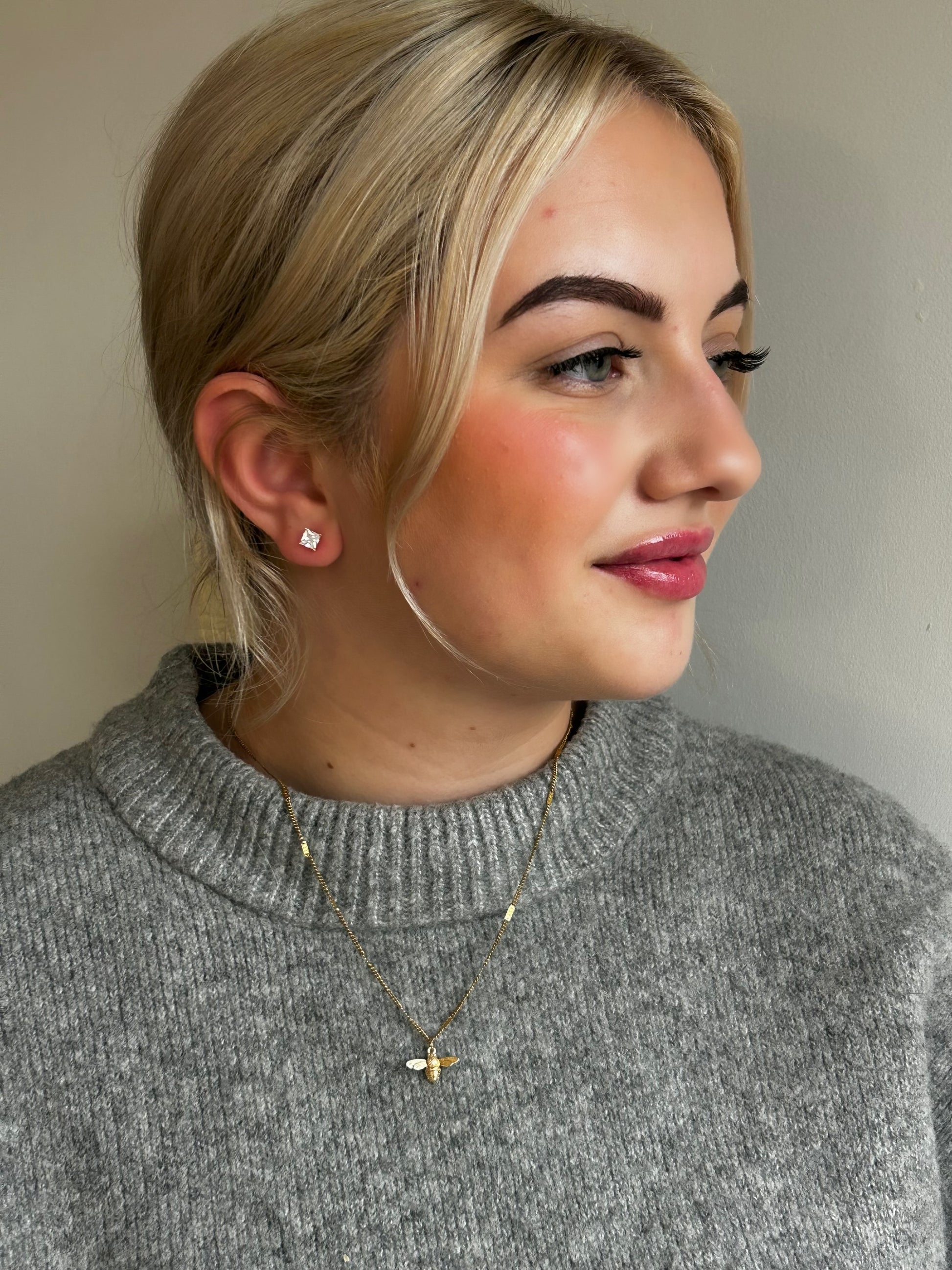 Woman wearing a gray sweater with a neutral background modelling Jessica and James jewellery bee necklace
