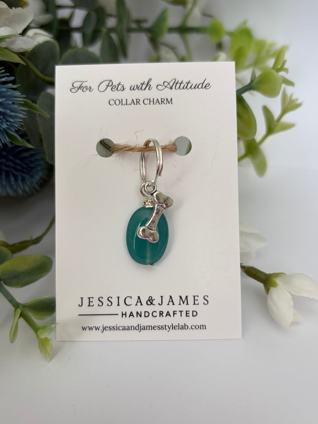 A handmade pet collar charm by Jessica & James, featuring a teal green teardrop bead and silver metal details, displayed on its white backing card with decorative green foliage.