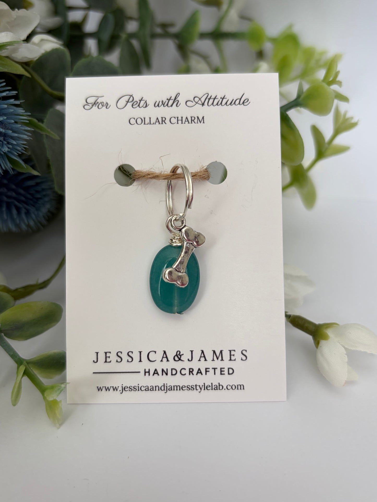 A handmade pet collar charm by Jessica & James, featuring a teal green teardrop bead and silver metal details, displayed on its white backing card with decorative green foliage.