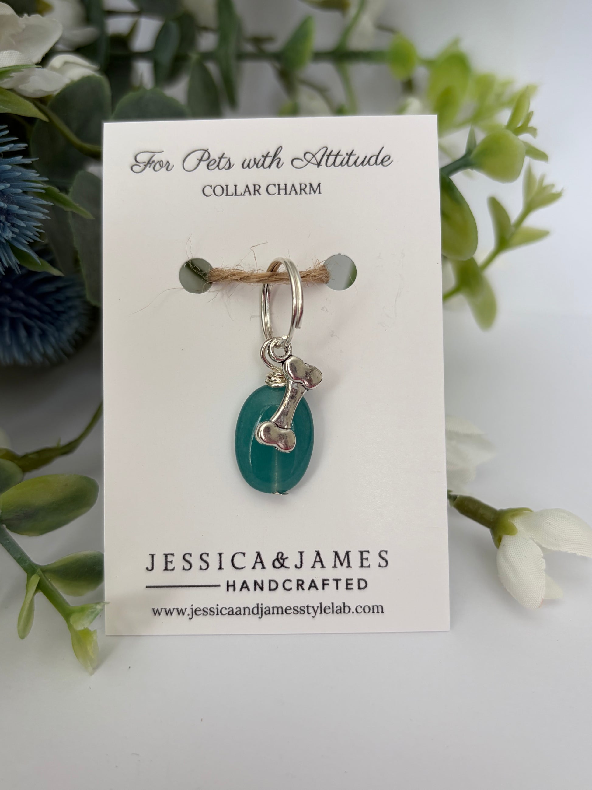 A handmade pet collar charm by Jessica & James, featuring a teal green teardrop bead and silver metal details, displayed on its white backing card with decorative green foliage.