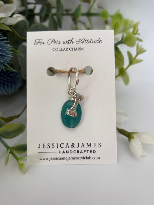 A handmade pet collar charm by Jessica & James, featuring a teal green teardrop bead and silver metal details, displayed on its white backing card with decorative green foliage.