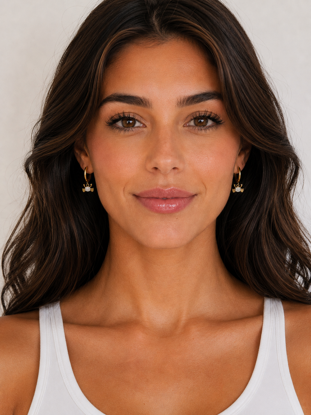 Woman wearing gold earrings with a neutral background