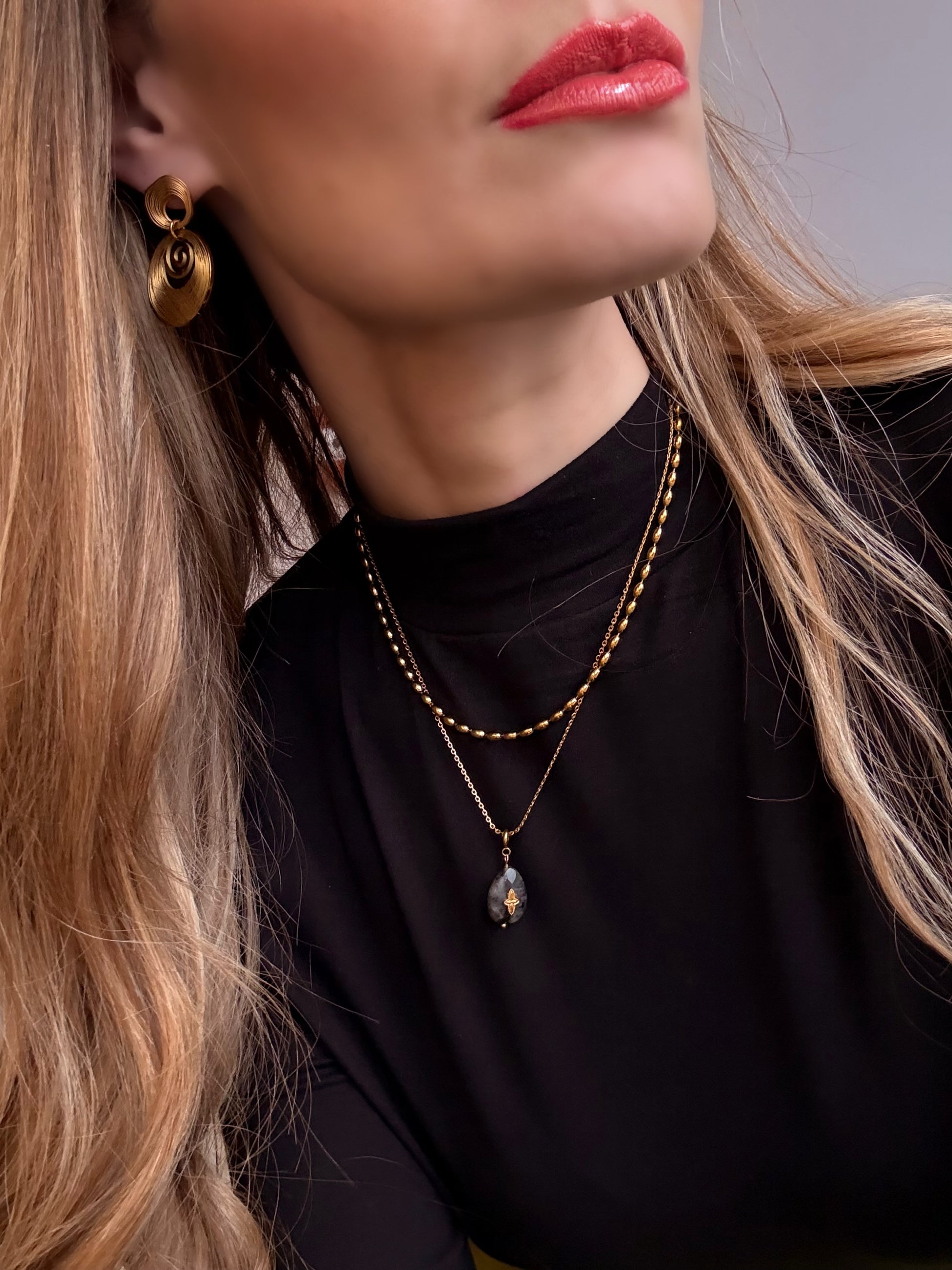 Close-up of a person wearing gold earrings and a necklace with a black background