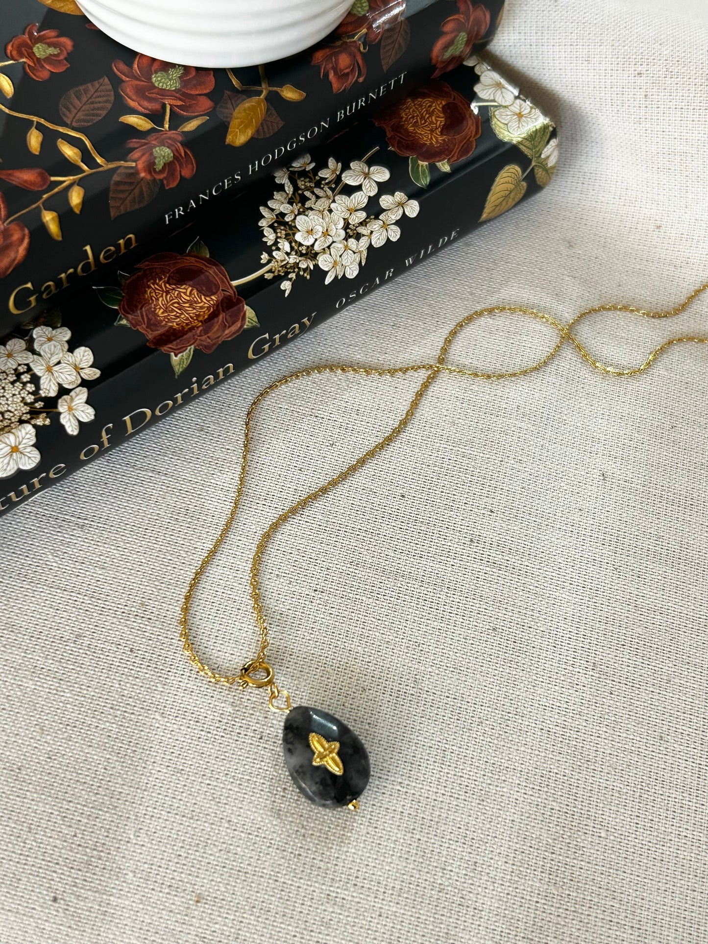 Gold necklace with a black cross pendant on a textured surface with books in the background
