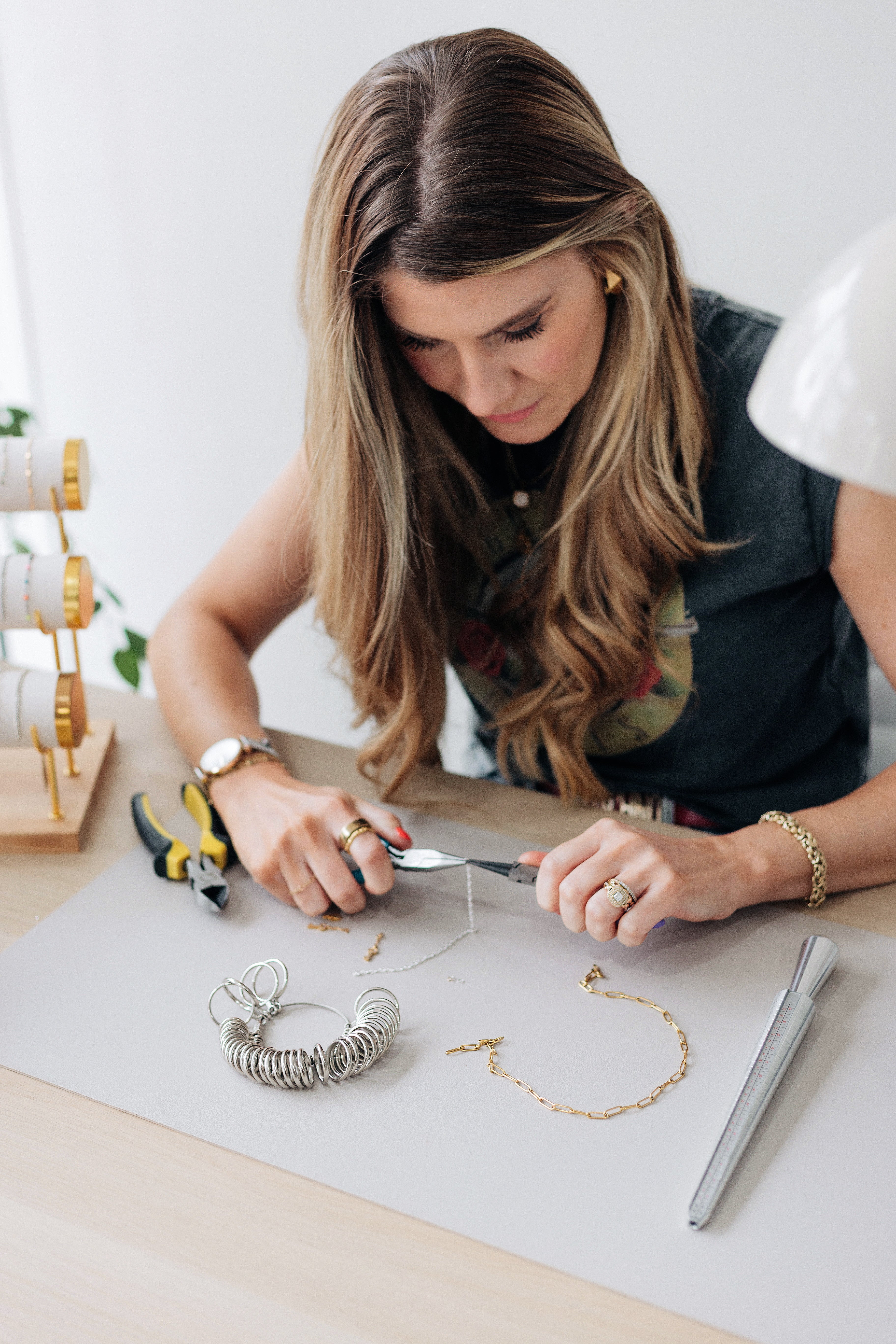 Woman working on jewelry at a table with tools and materials.