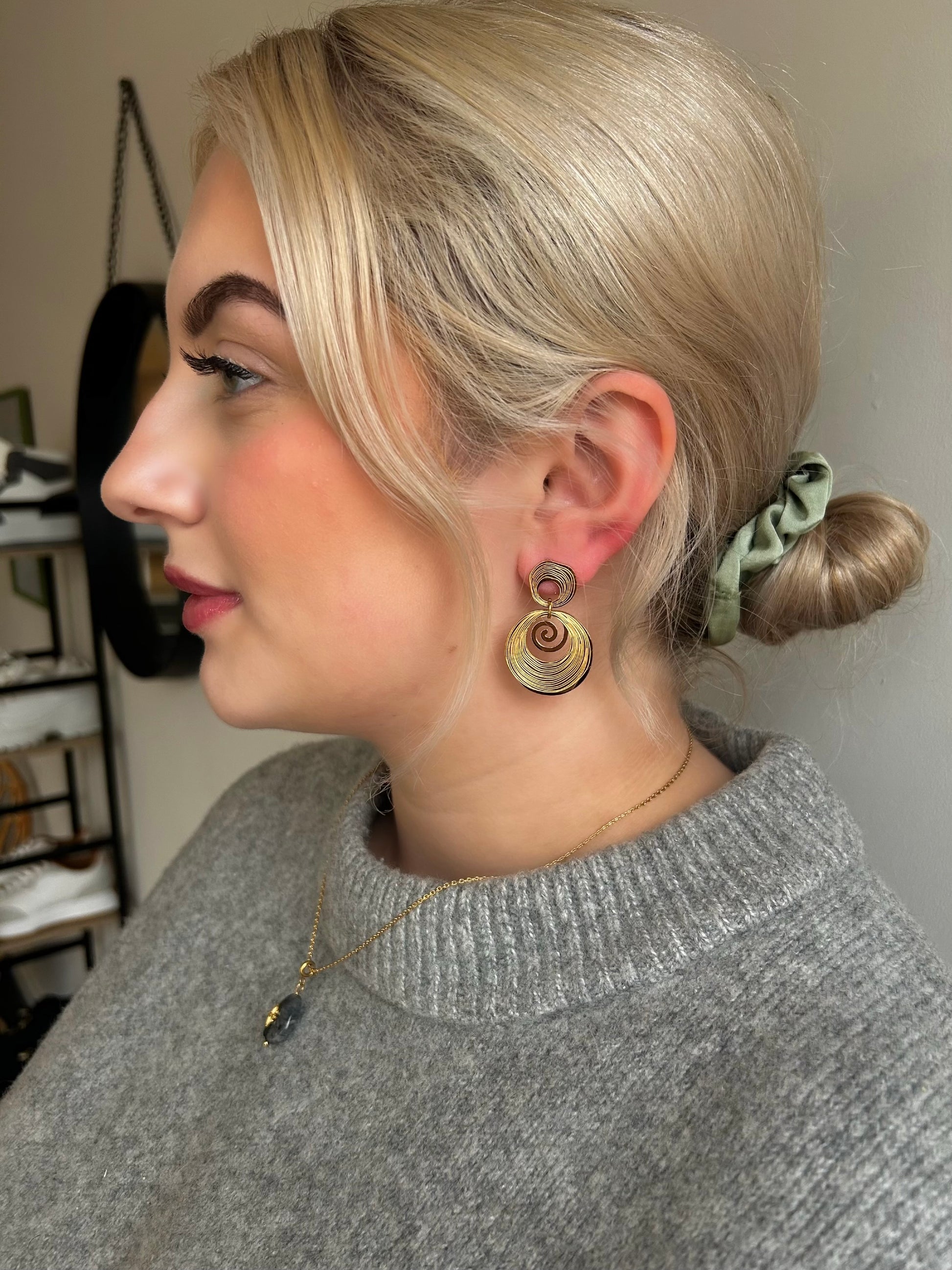Woman with styled hair and earrings, wearing a gray sweater.