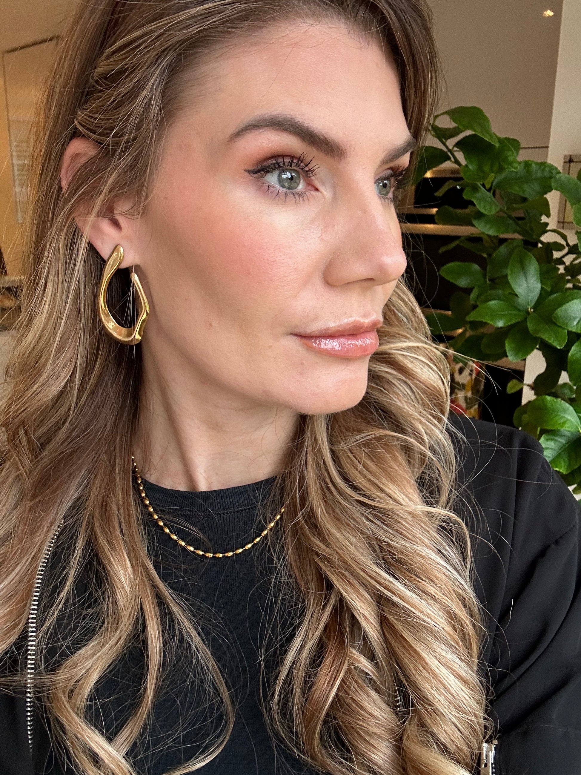 Close-up of a woman with blonde hair and gold earrings indoors.