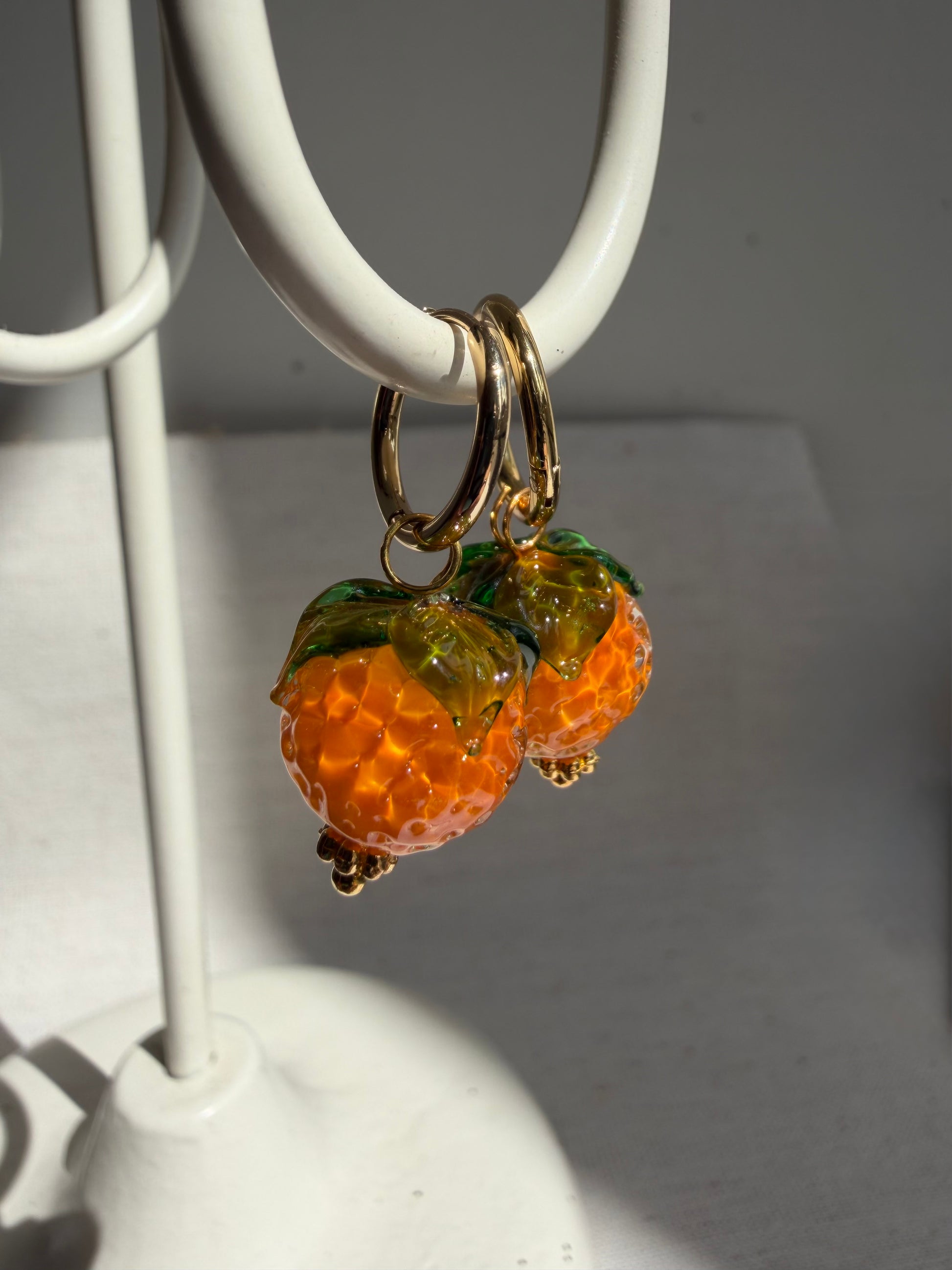 Orange Fruit earrings on a white stand with a neutral background