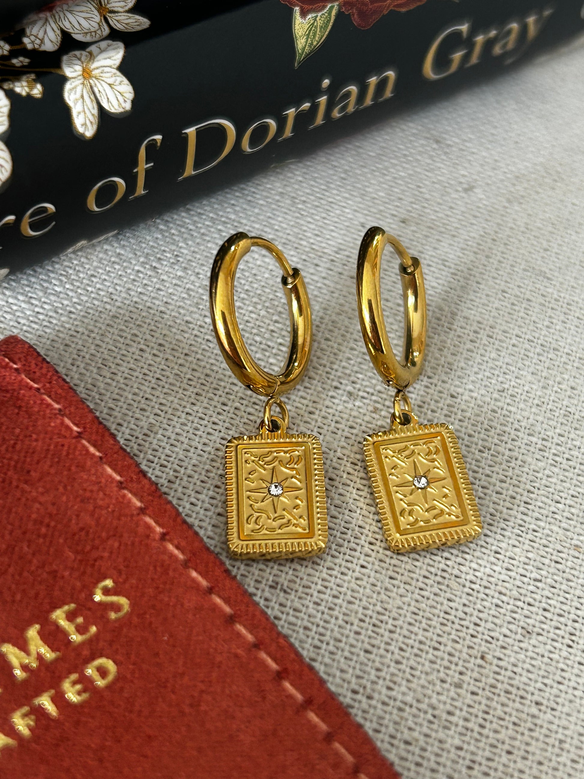 Gold hoop earrings with intricate designs on a textured fabric background