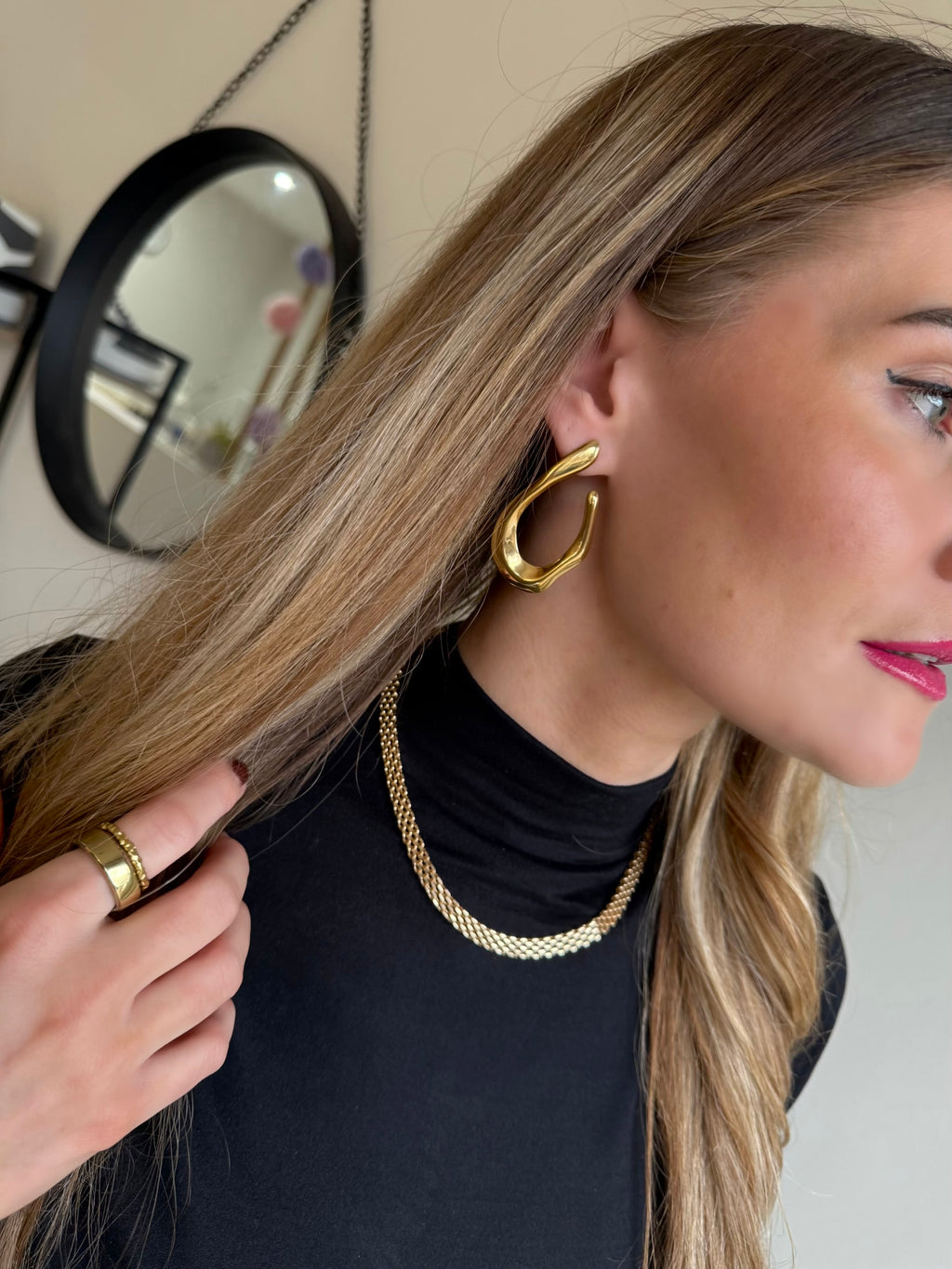 Woman wearing gold hoop earrings and a gold necklace, with a mirror in the background.