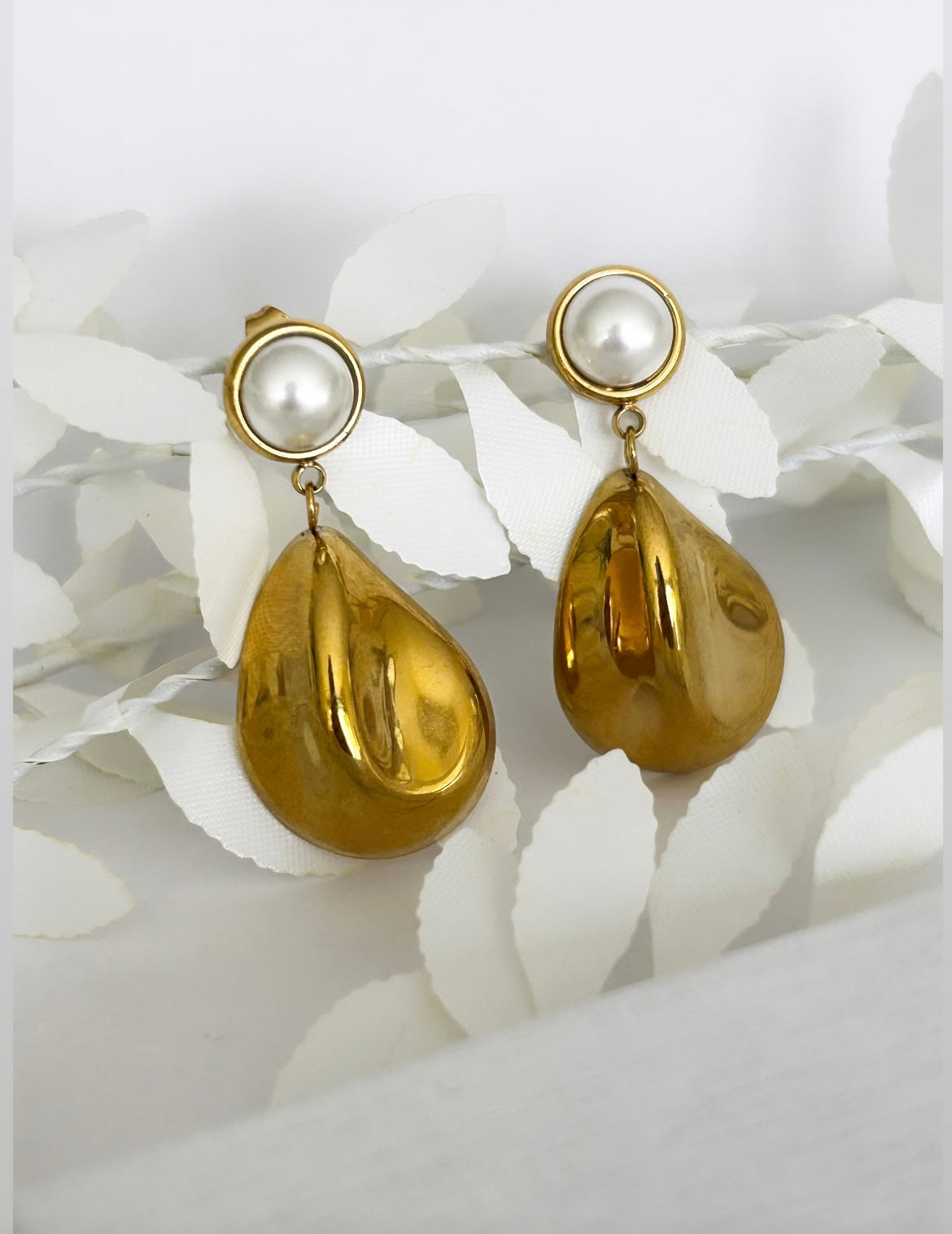 Gold earrings with pearl-like tops on a white leaf background