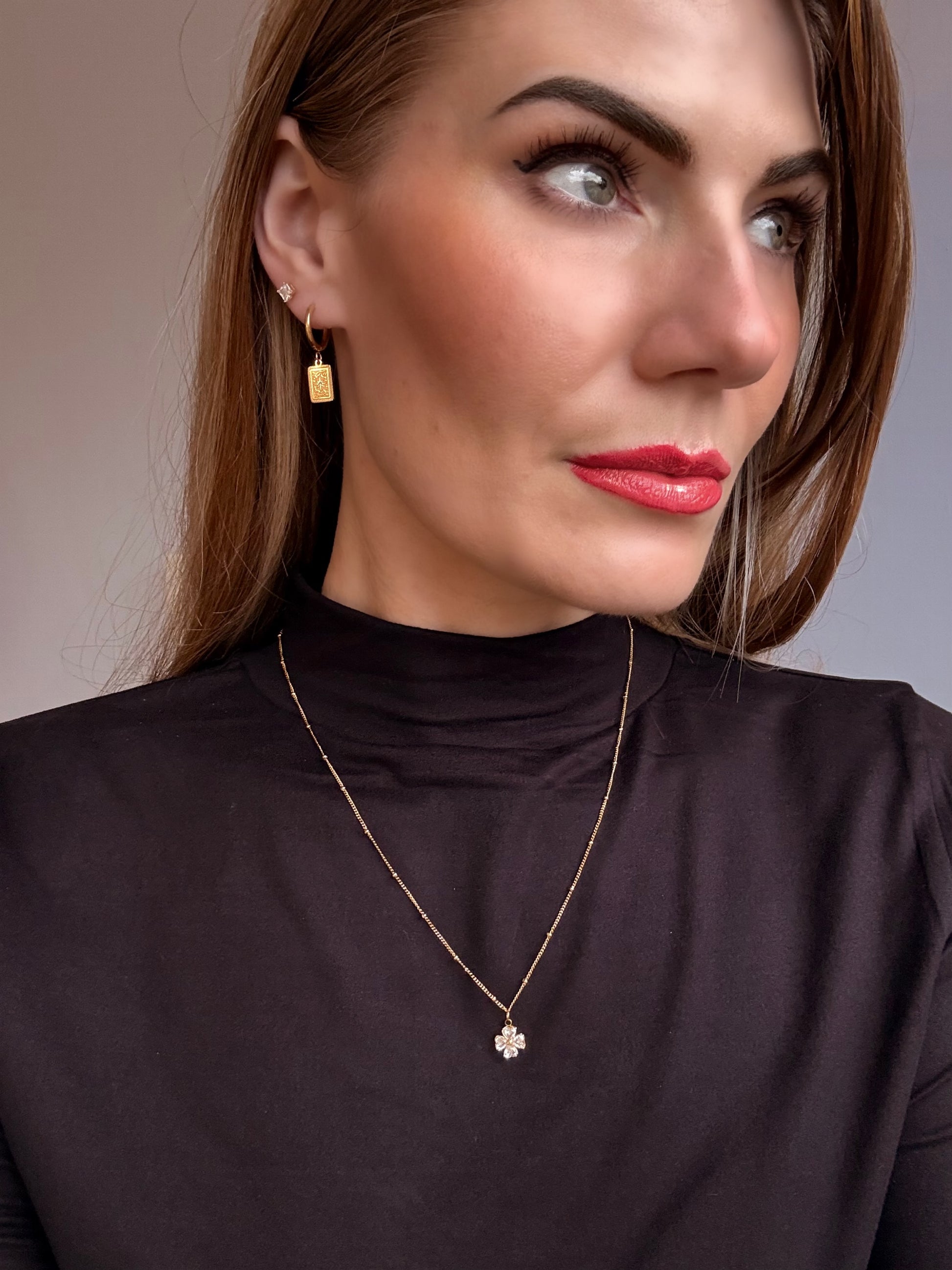Woman wearing a gold necklace and earrings against a neutral background