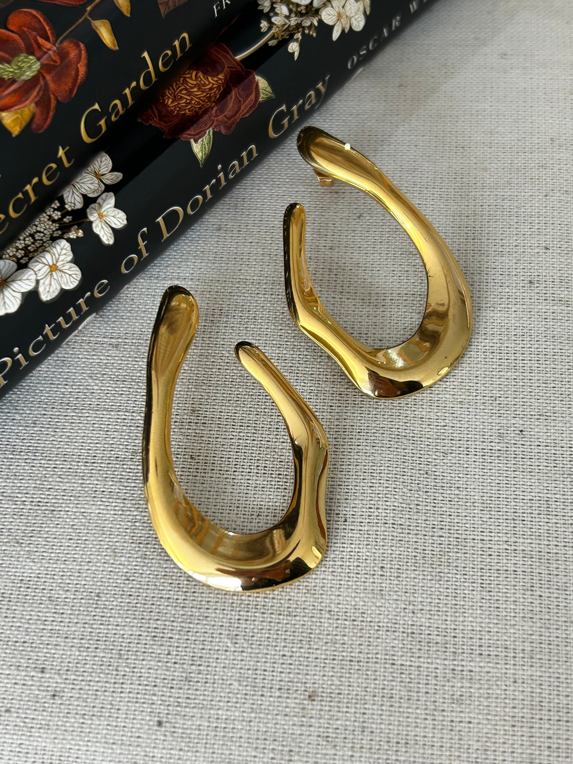 Gold earrings on a textured surface with a book in the background