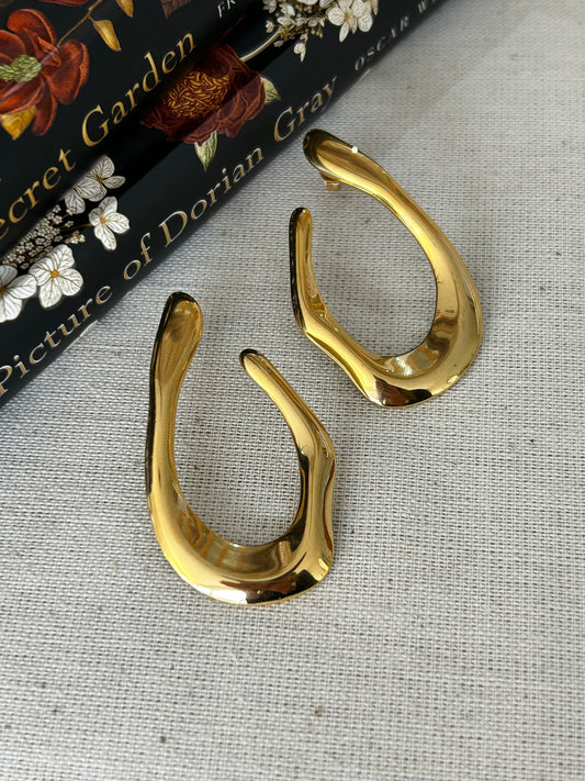 Gold earrings on a textured surface with a book in the background